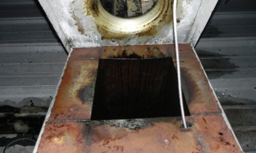 Close-up of a greasy, rust-stained metal vent or duct opening with visible grime and residue around the edges.