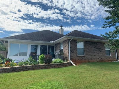 Single-story brick house with a landscaped garden, patio furniture, and a well-maintained lawn under a partly cloudy sky.