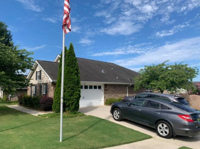 A brick suburban house with a two-car garage, two parked cars, and an American flag on a sunny day.