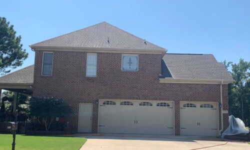 Two-story brick house with three-car garage, concrete driveway, and manicured lawn on a sunny day.