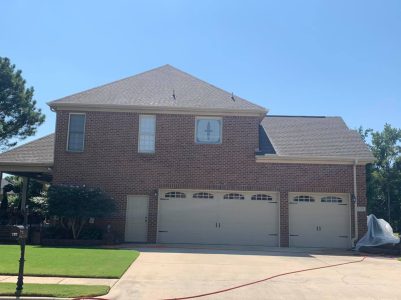 Two-story brick house with three-car garage, concrete driveway, and manicured lawn on a sunny day.