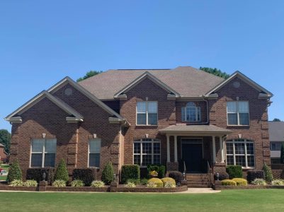 Two-story brick house with large windows, landscaped front yard, and symmetrical architectural design under a clear sky.