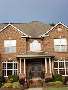 Two-story brick house with large windows, dark double front doors, and landscaped shrubs along the entry steps.