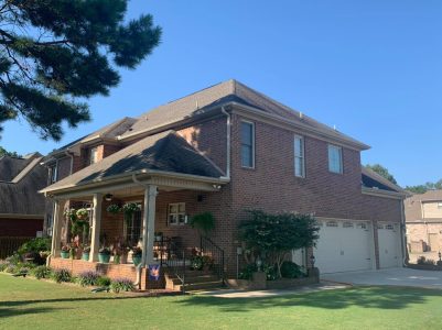 Two-story brick house with a covered front porch, attached three-car garage, and landscaped yard on a sunny day.