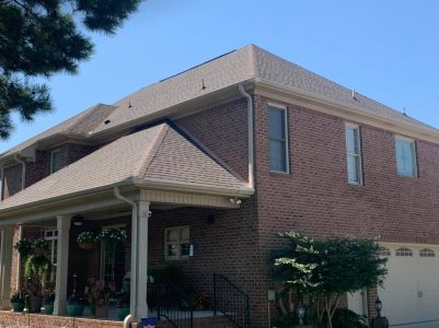 Two-story red brick house with a covered front porch, beige trim, and attached garage under a clear blue sky.