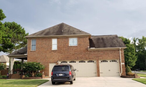 A black minivan is parked in the driveway of a two-story brick house with three garage doors.