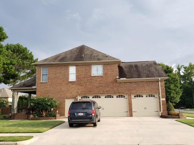 A black minivan is parked in the driveway of a two-story brick house with three garage doors.