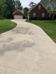 A curved concrete driveway leads to a brick house with a two-car garage and a well-maintained lawn.