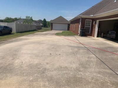 Concrete driveway leading to a detached garage, with a house and an open garage door on the right side.