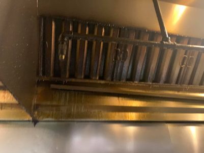 Close-up of a commercial kitchen vent hood with visible grease buildup and grime on the surfaces.