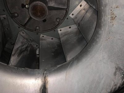 Close-up view of a metal industrial fan with visible dirt and wear on the blades and surrounding surface.