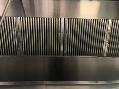 A close-up view of a stainless steel commercial kitchen exhaust hood with metal grease filters installed.