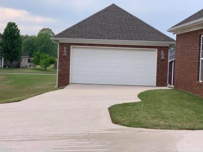 A brick garage with a closed white door, bordered by a concrete driveway and trimmed grass, on a cloudy day.