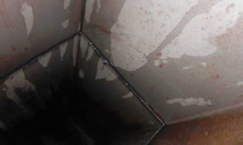Close-up view of the inside corner of a metal vent or duct with rust, discoloration, and water stains on the surface.