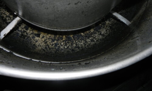 Close-up of a metal surface with dark spots and residue, possibly grease or grime buildup, around the base of a machine.