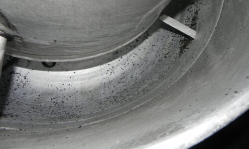 Close-up view of the interior of a metal industrial container with scattered black particles.