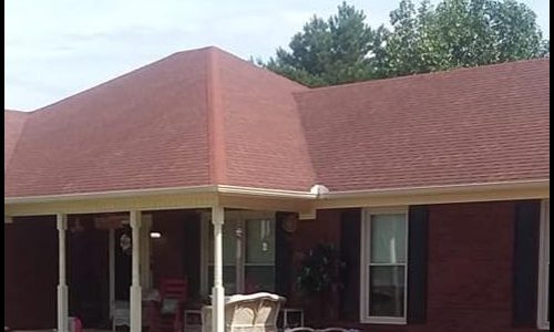 Single-story red brick house with a red roof, front porch, white columns, and outdoor furniture.