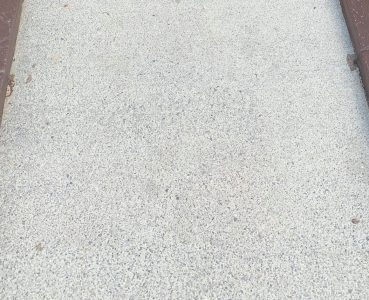 Concrete sidewalk with a rough, speckled surface bordered by two rust-colored metal rails on either side.